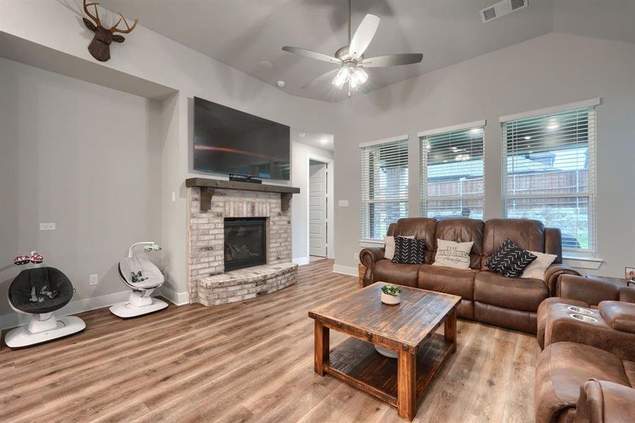 Living room with a brick fireplace, light hardwood / wood-style flooring, vaulted ceiling, and ceiling fan