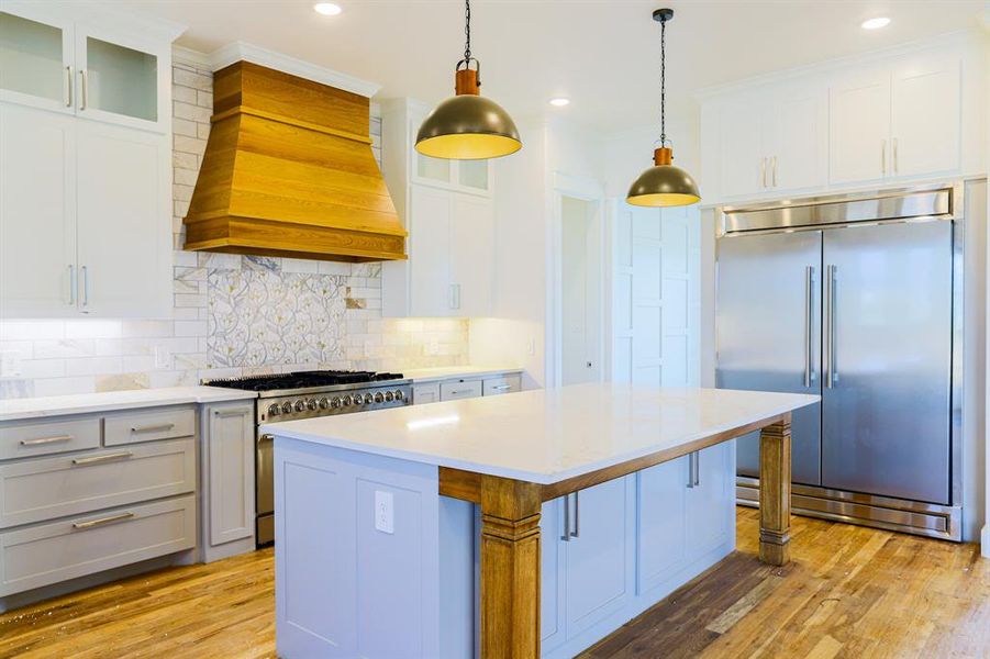 Kitchen with light hardwood / wood-style floors, custom exhaust hood, high end appliances, and a kitchen island