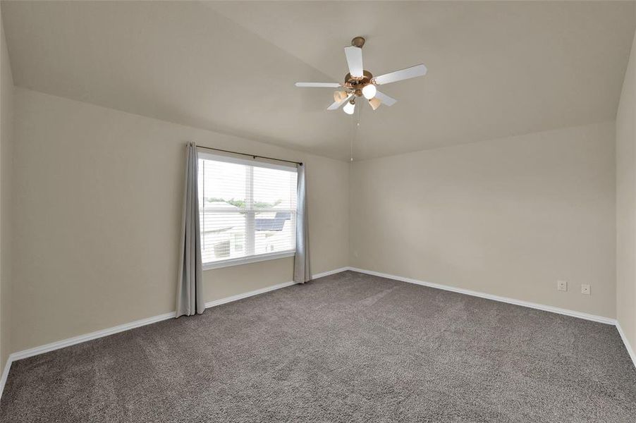 This is a spacious, well-lit Primary  bedroom with a vaulted ceiling, featuring a ceiling fan, neutral walls, and carpeted flooring. A large window offers natural light and a view of the exterior.