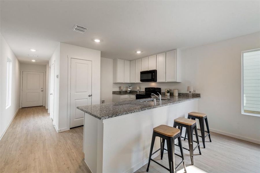 Kitchen with kitchen peninsula, black appliances, a kitchen breakfast bar, dark stone countertops, and light hardwood / wood-style floors