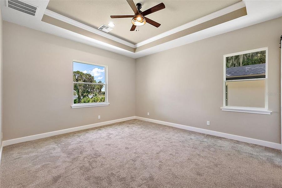 Owner's bedroom with ceiling fan, tray ceiling with crown, and cozy, brand new carpet