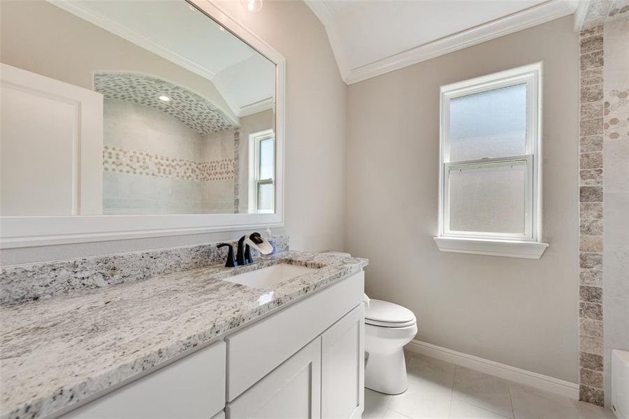 Bathroom with tiled shower, plenty of natural light, vanity, and toilet