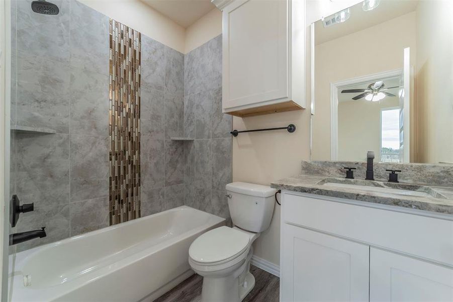 Full bathroom with tiled shower / bath, hardwood / wood-style flooring, toilet, ceiling fan, and vanity