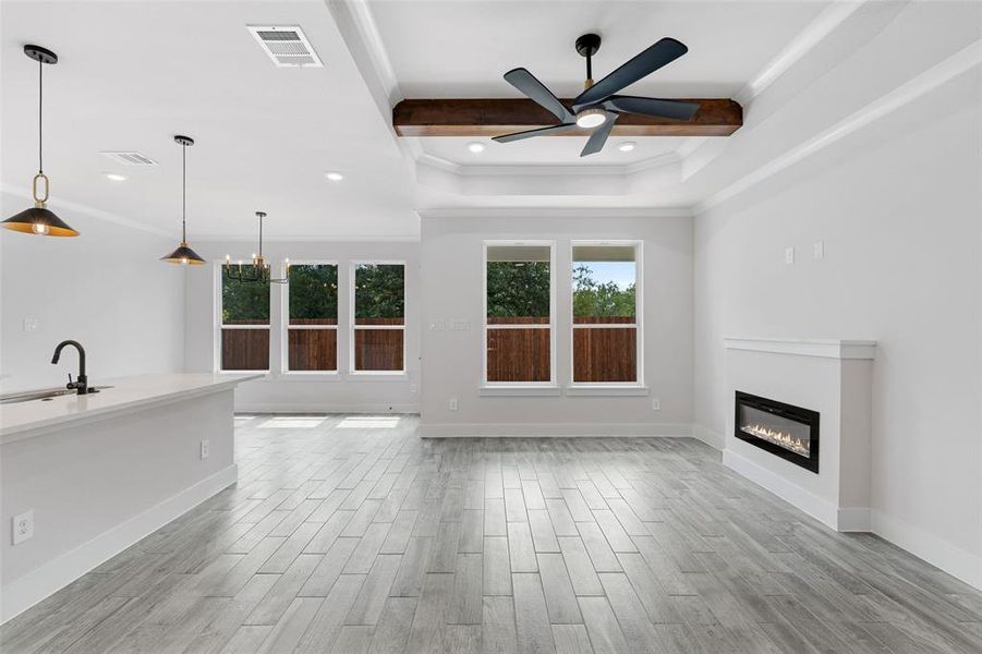 Unfurnished living room featuring ornamental molding, sink, ceiling fan, a raised ceiling, and light hardwood / wood-style floors