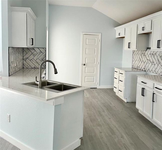 Kitchen with backsplash, sink, light hardwood / wood-style floors, and white cabinets