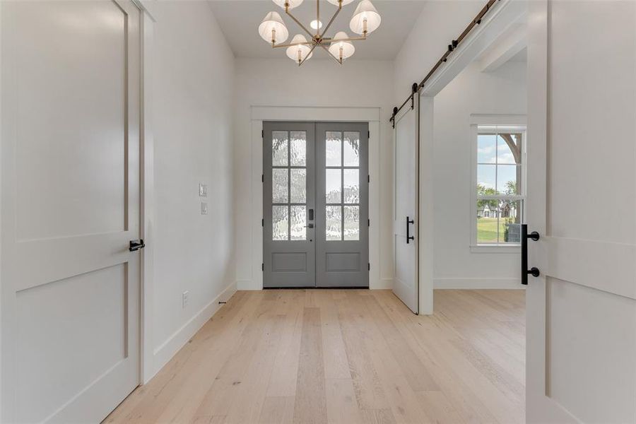 Foyer featuring light hardwood / wood-style flooring, a barn door, french doors, and a chandelier