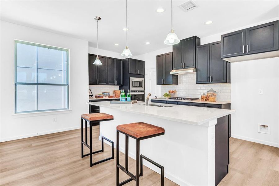 Kitchen with sink, hanging light fixtures, stainless steel appliances, and light hardwood / wood-style floors