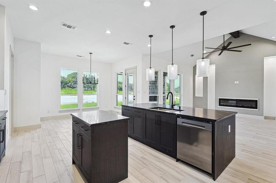 Kitchen featuring light wood-type flooring, ceiling fan with notable chandelier, sink, an island with sink, and stainless steel dishwasher