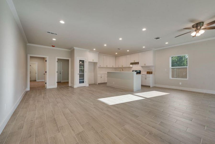 Unfurnished living room with light hardwood / wood-style floors, ornamental molding, and ceiling fan