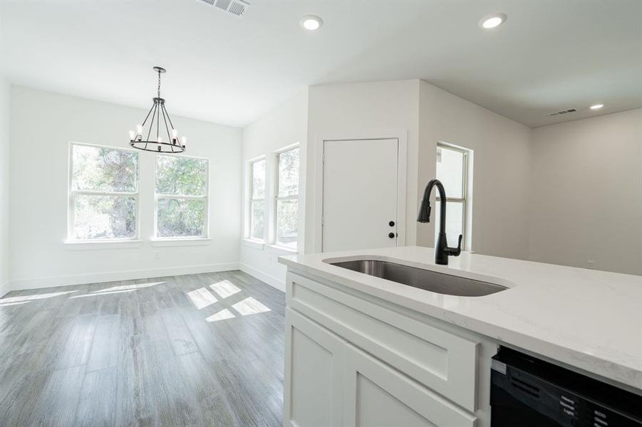 Kitchen with light wood-type flooring, white cabinetry, dishwasher, light stone counters, and sink