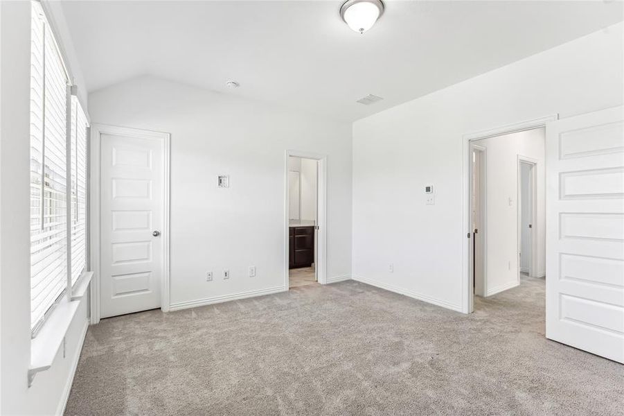 Unfurnished bedroom featuring light colored carpet, connected bathroom, and vaulted ceiling