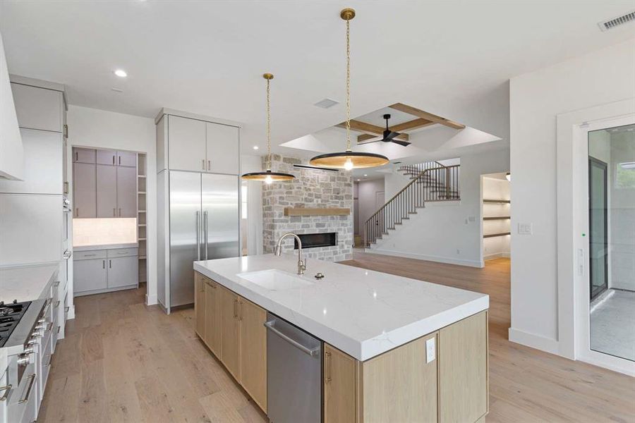 Kitchen featuring sink, a stone fireplace, a large island, appliances with stainless steel finishes, and light hardwood / wood-style floors