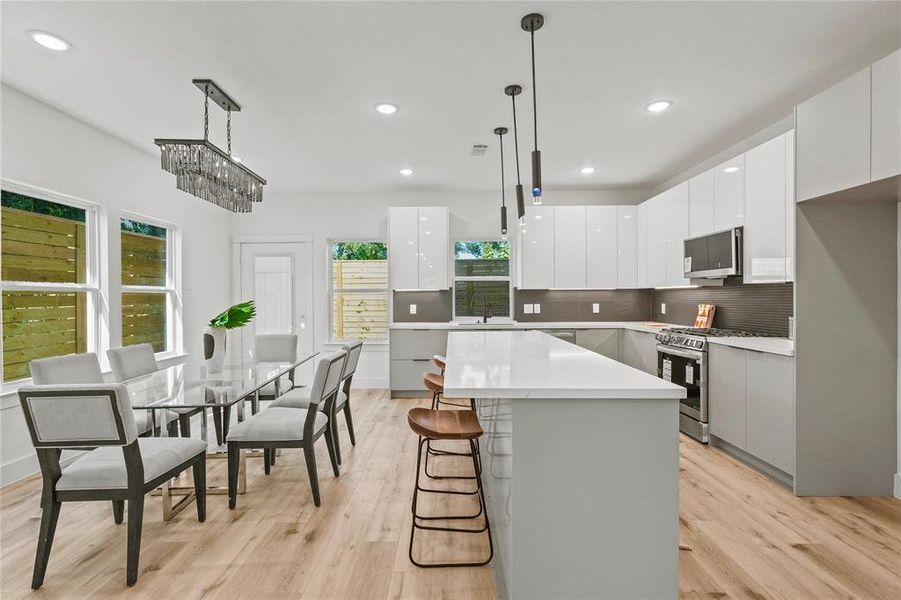 Kitchen with appliances with stainless steel finishes, hanging light fixtures, light hardwood / wood-style flooring, and white cabinets