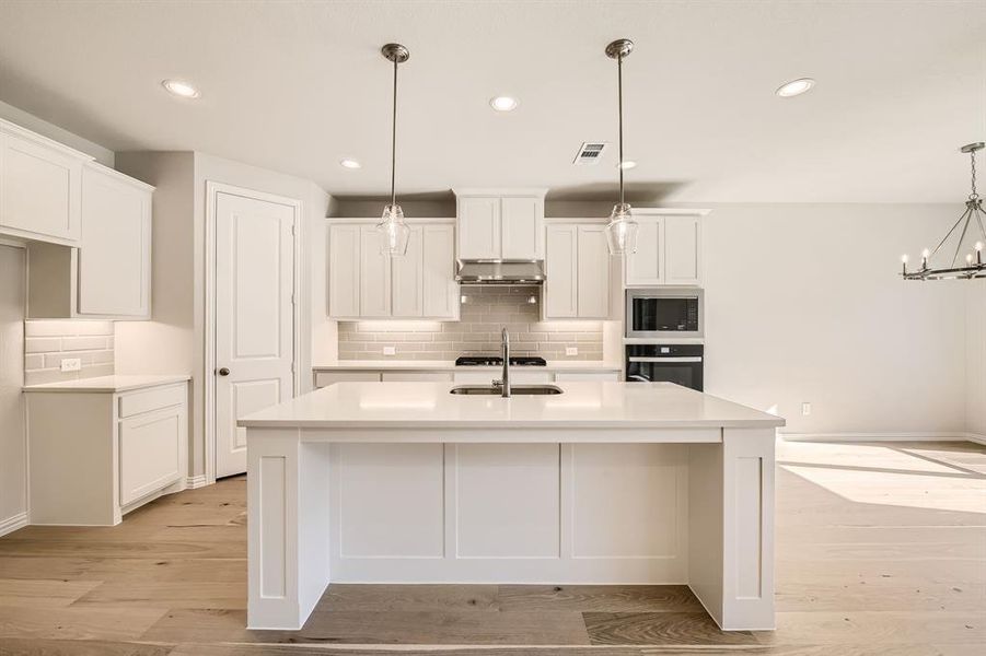 Kitchen featuring an island with sink, backsplash, decorative light fixtures, appliances with stainless steel finishes, and light hardwood / wood-style floors