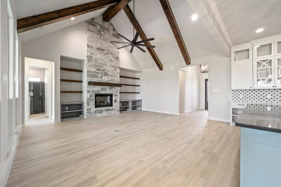 Unfurnished living room featuring light hardwood / wood-style floors, beam ceiling, a fireplace, and high vaulted ceiling