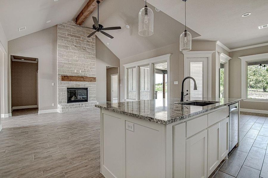 Kitchen featuring white cabinets, a center island with sink, a large fireplace, beam ceiling, and ceiling fan