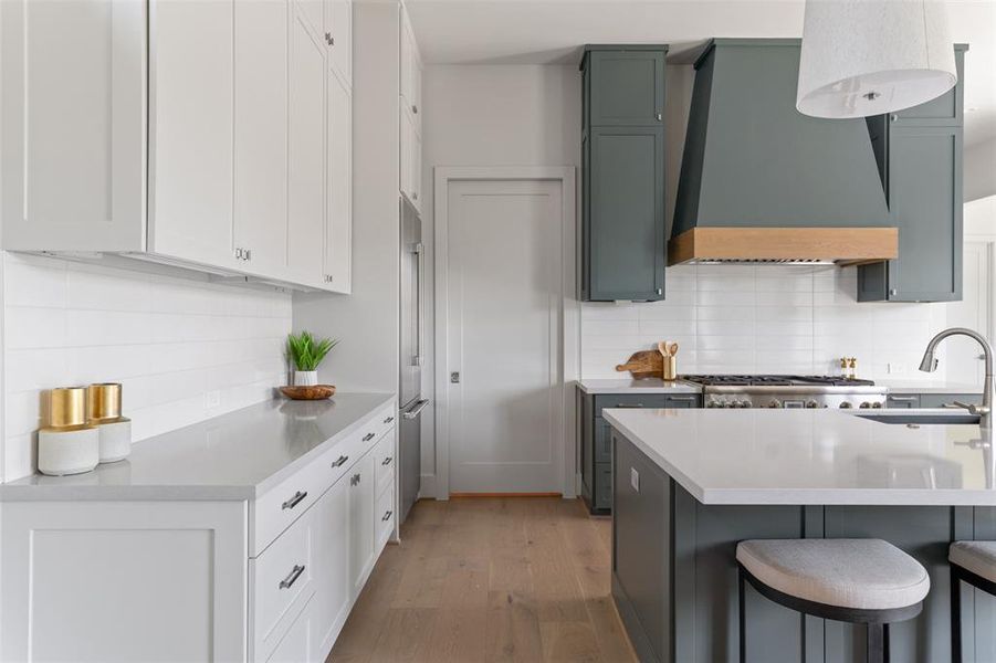 This is a modern kitchen with white and contrasting darker cabinetry, stainless steel appliances, a stylish backsplash, and a center island with bar seating. The space is well-lit and features clean lines and contemporary finishes.