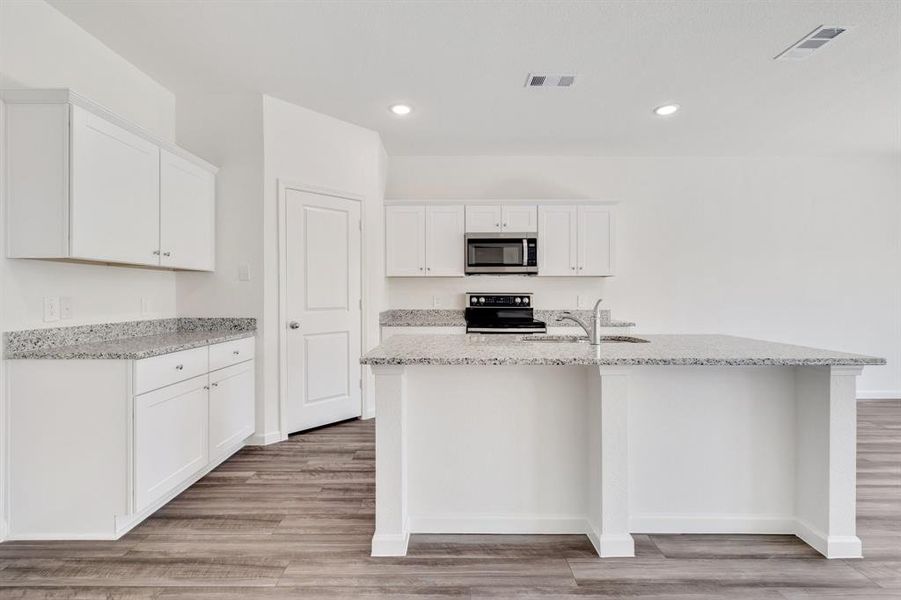 Kitchen with light hardwood / wood-style floors, white cabinetry, stove, a kitchen island with sink, and sink