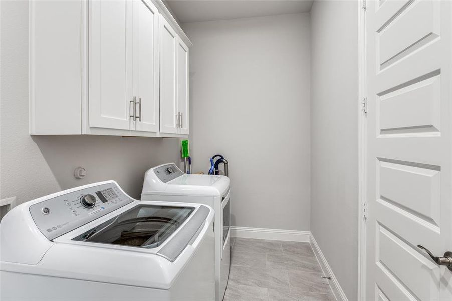 Laundry area with cabinets, independent washer and dryer, and light tile patterned floors