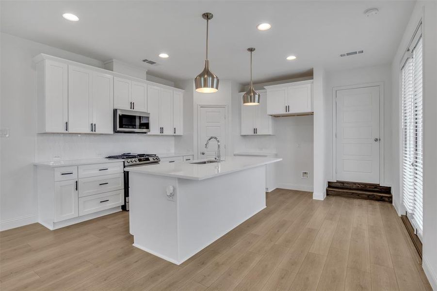 Kitchen featuring light hardwood / wood-style floors, stainless steel appliances, a healthy amount of sunlight, white cabinetry, and an island with sink