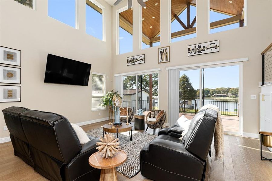 Living room with a towering ceiling, ceiling fan, a water view, and light hardwood / wood-style flooring