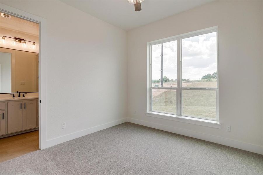 Unfurnished bedroom with sink, ensuite bath, light colored carpet, and ceiling fan