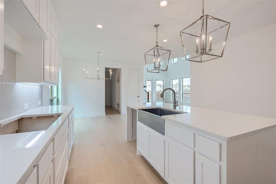 Kitchen with light stone counters, a center island with sink, decorative light fixtures, and sink