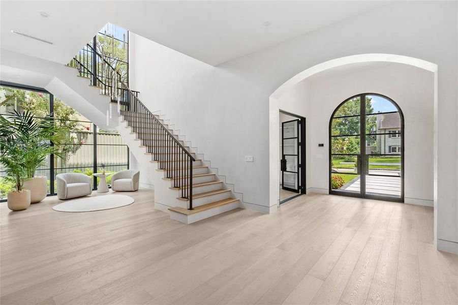 Floor-to-ceiling windows flood this space with natural light, illuminating both the first and second floors with a captivating ambiance. A bespoke modern chandelier hangs overhead, while a graceful custom iron railing adds a touch of refinement.