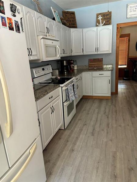 Kitchen with light hardwood / wood-style flooring, dark stone counters, white appliances, and white cabinetry