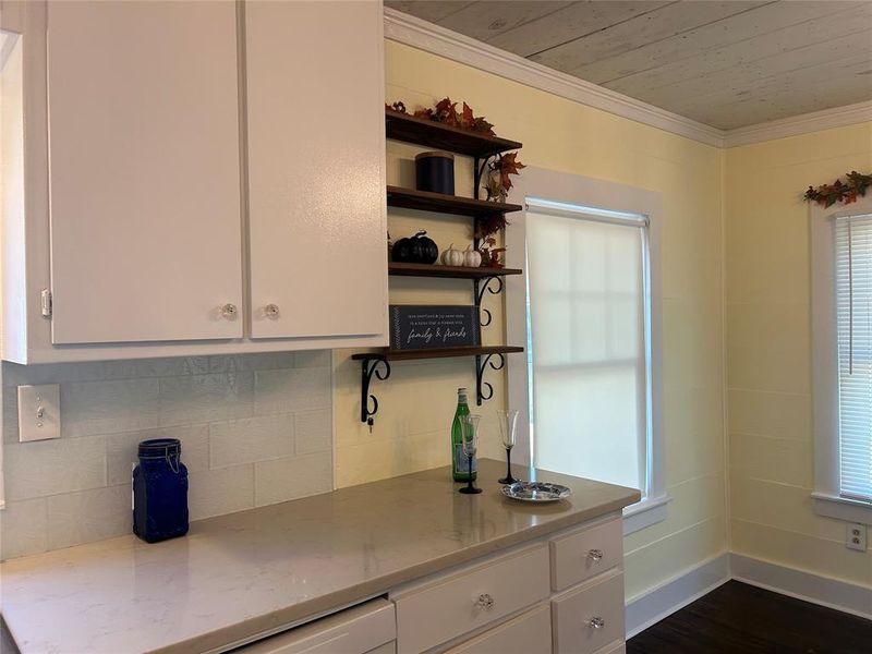 Kitchen featuring dark wood-type flooring, crown molding, light stone countertops, white cabinets, and tasteful backsplash