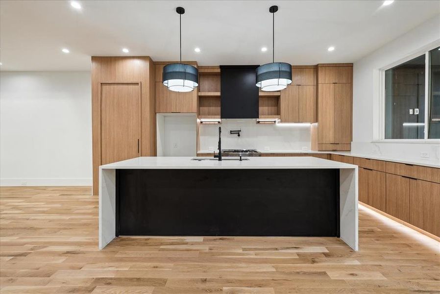 Kitchen featuring decorative light fixtures, sink, a kitchen island with sink, and light hardwood / wood-style flooring