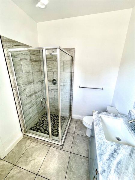 Bathroom featuring tile patterned floors, toilet, a shower with door, and vanity