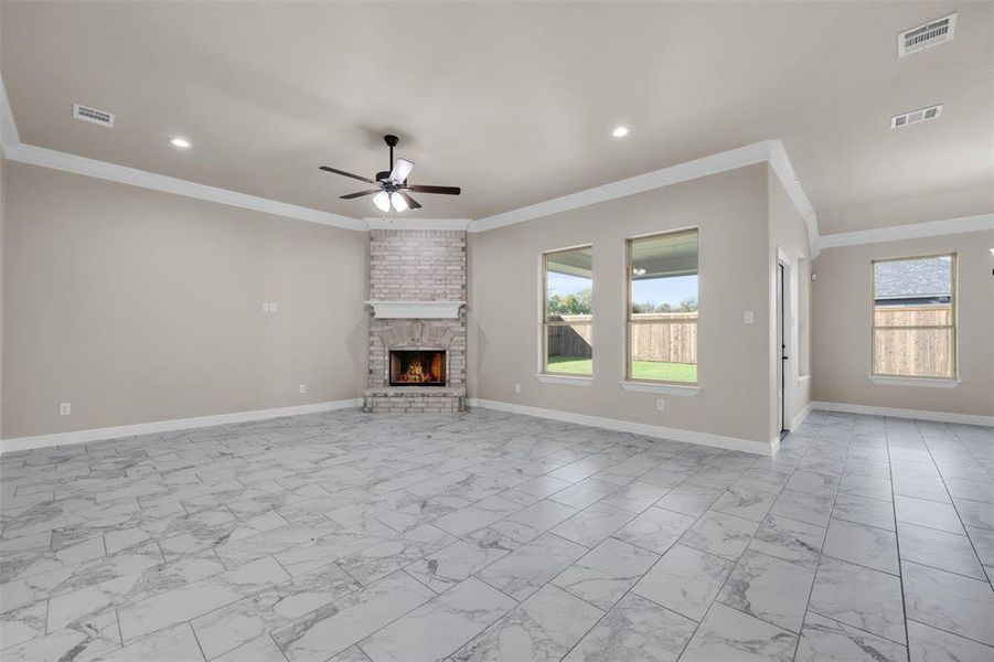 Unfurnished living room featuring a brick fireplace, ceiling fan, and crown molding