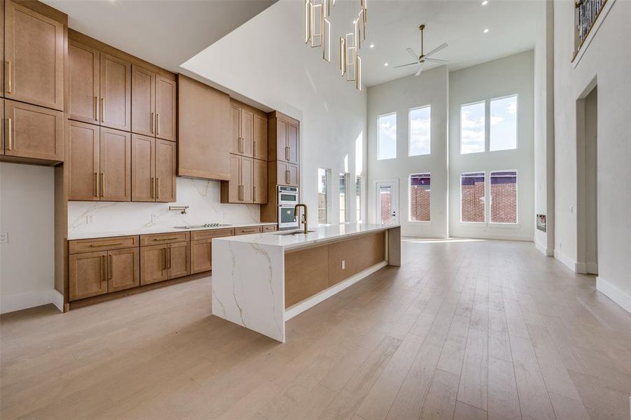 Kitchen with a kitchen island with sink, cooktop, a towering ceiling, light stone counters, and light hardwood / wood-style floors