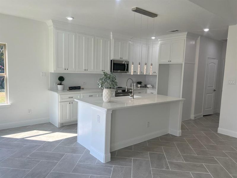 Kitchen featuring sink, decorative light fixtures, a kitchen island with sink, white cabinetry, and decorative backsplash