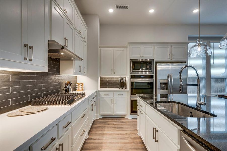 Kitchen with appliances with stainless steel finishes, light hardwood / wood-style flooring, sink, hanging light fixtures, and backsplash