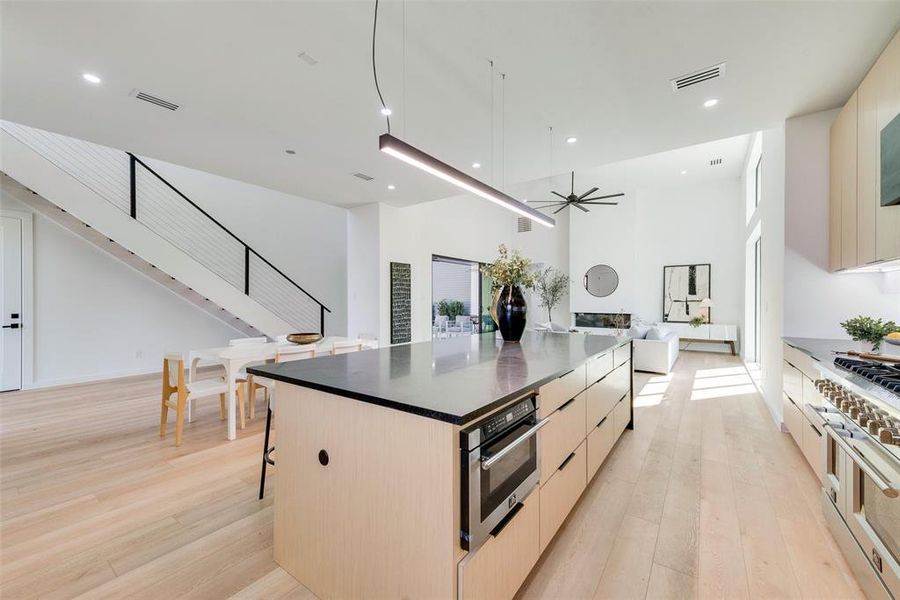 Kitchen with a kitchen breakfast bar, stainless steel appliances, light wood-type flooring, a high ceiling, and a center island