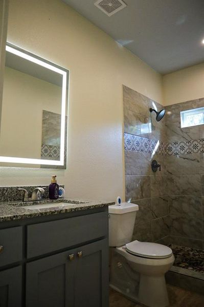 Bathroom featuring vanity, hardwood / wood-style flooring, toilet, and a tile shower