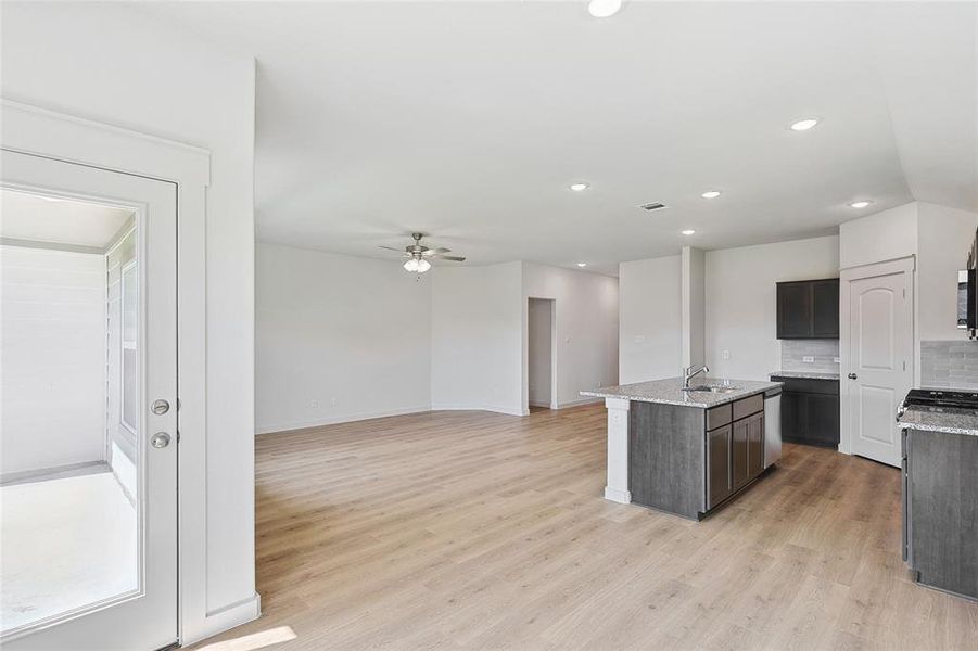 Kitchen featuring ceiling fan, an island with sink, sink, light hardwood / wood-style flooring, and decorative backsplash