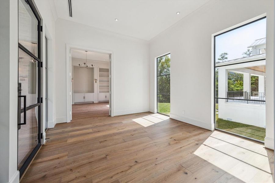 This grand entryway, framed by sleek steel windows and a striking front door, offers a stunning view of the expansive back lawn. The wide, open space provides the perfect setting to showcase impressive artwork, making a bold first impression. To the left, you'll find the first-floor study, creating a seamless blend of elegance and functionality.