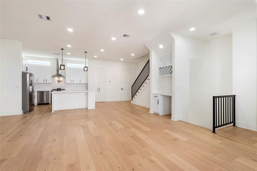 Modern open-plan living space with a bright kitchen featuring stainless steel appliances and white cabinetry. Elegant hardwood floors throughout, leading to an inviting staircase.