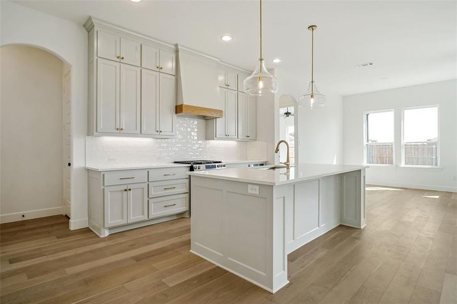 Kitchen with custom range hood, sink, an island with sink, and white cabinets