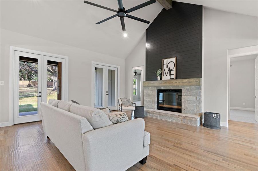 Living room featuring light hardwood / wood-style flooring, a stone fireplace, high vaulted ceiling, and plenty of natural light