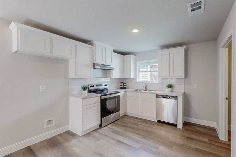 Kitchen with white cabinets, stainless steel appliances, sink, and light hardwood / wood-style flooring