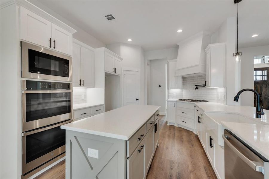 Kitchen featuring decorative light fixtures, tasteful backsplash, white cabinets, appliances with stainless steel finishes, and light hardwood / wood-style flooring