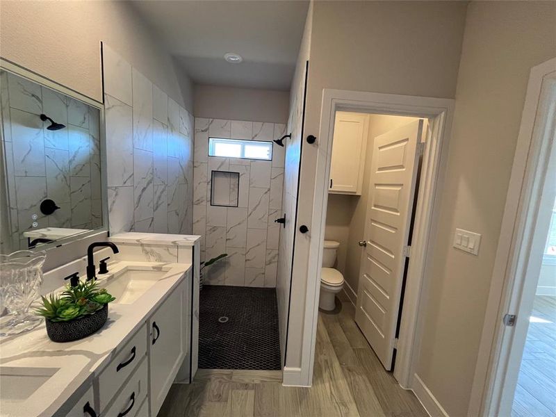 Bathroom featuring hardwood / wood-style floors, toilet, vanity, and tiled shower