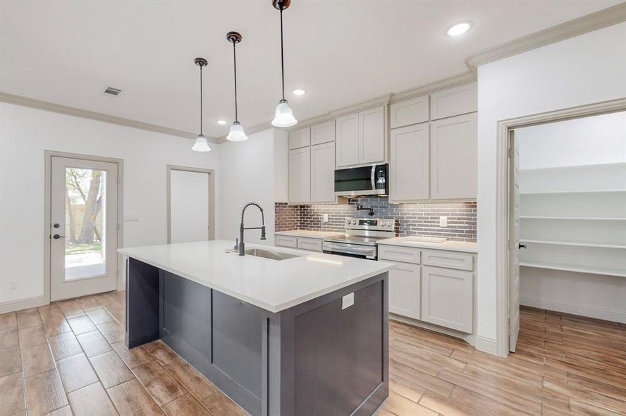 Kitchen with appliances with stainless steel finishes, a center island with sink, sink, pendant lighting, and decorative backsplash
