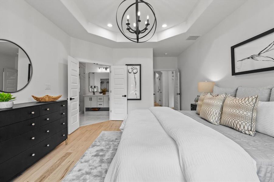 Bedroom with light hardwood / wood-style flooring, a raised ceiling, and a chandelier