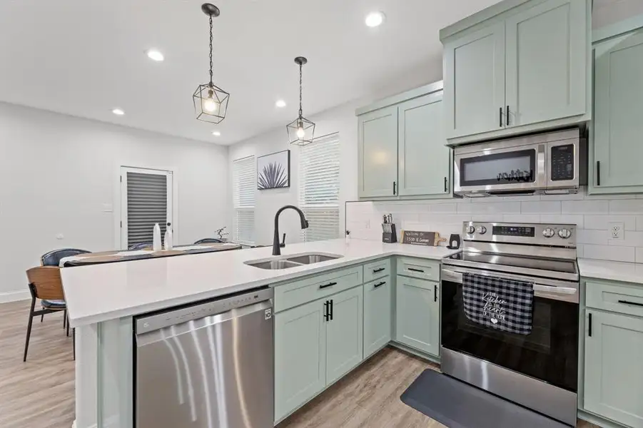 Kitchen with green cabinets, hanging light fixtures, stainless steel appliances, and sink