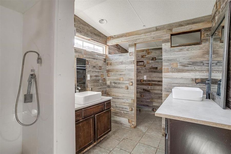 Bathroom with lofted ceiling, wooden walls, a textured ceiling, and vanity